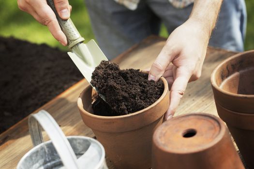 Hands putting soil to a clay flower pot