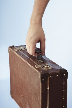 A Hand carrying an old brown suitcase