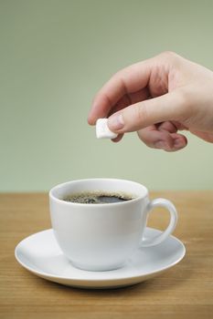 A Hand adding sugar to a cup of black coffee