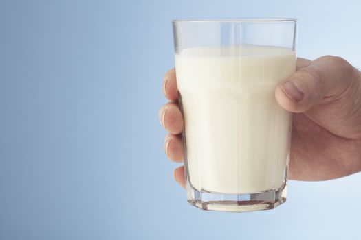 A Hand holding a glass of milk. Copy space on the left.