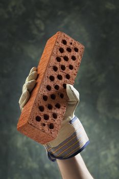 Hand with protective glove holding a new perforated brick.