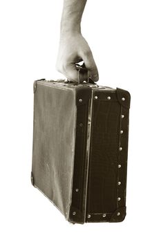 Sepia toned photograph of a hand holding an old suitcase. Short depth-of-field, the sharpness is in the hand.