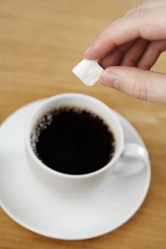 A Hand putting a sugar cube into a cup of coffee.