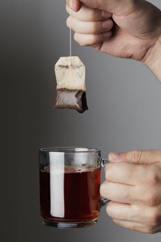 Hand lifting a wet used tea bag from a glass tea mug