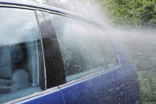 Water spray from hose on a blue car