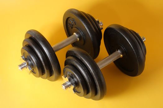 A Pair of iron dumbells on a yellow surface