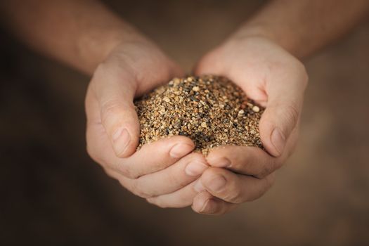 Man holding coarse sand in his cupped hands.