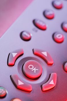 Digital television remote control buttons in red light.