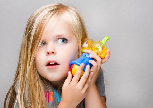 Young girl trying to use a toy hammer as a phone or just having fun playing make believe