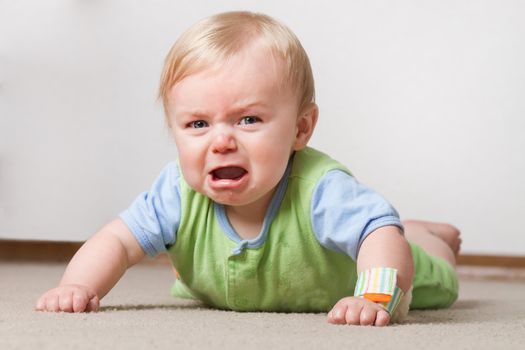 A young baby having a fit on the ground crying and making a pout face