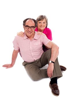 Smiling senior couple seated on floor. Posing against white background