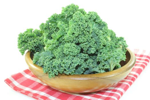 fresh green kale in a wood bowl on a napkin in front of a light background