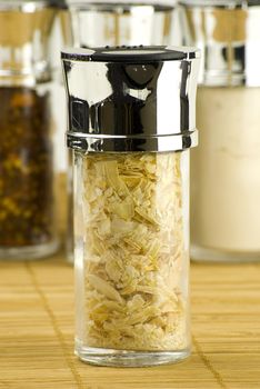 dry onion flakes in a glass jar on different spices background over wooden mat