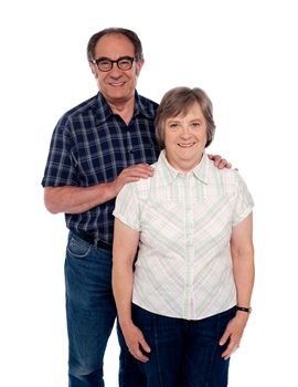 Aged love couple posing with smile. Male resting hands on her woman from behind
