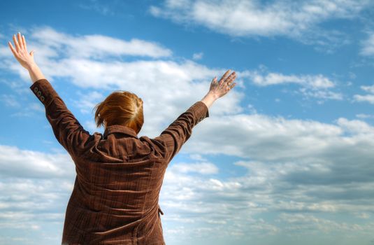 Woman with raised hands against blue sky