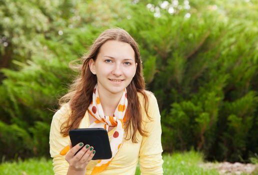 Teen girl reading an electronic book outdoors