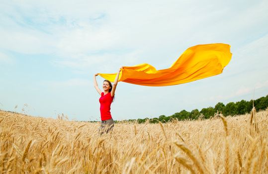 Teen girl with yellow fabric at the wheat field in sunny day