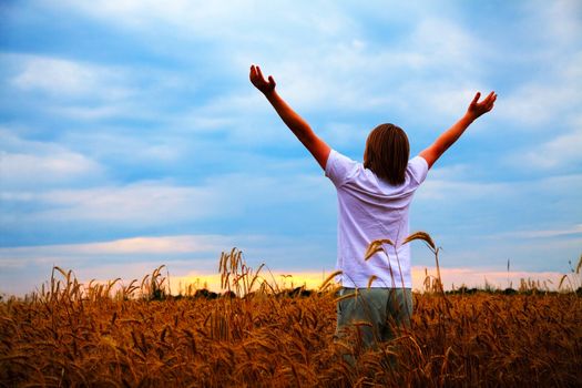 Young man staying with raised at wheat field hands at sunset time