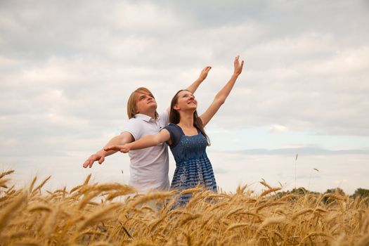 Couple staying with raised at wheat field hands at sunset time