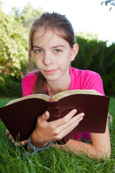 Teen girl reading the Bible outdoors lying on the grass