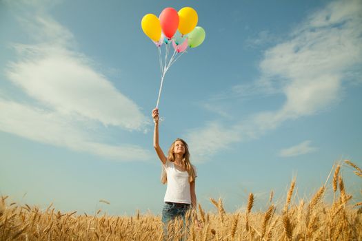 Teen girl at a wheat field with balloons in sunny day