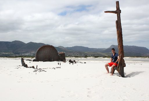 Man sitting at Shipwreck Kakapo at the beach of kommetjie with upcoming storm in the background