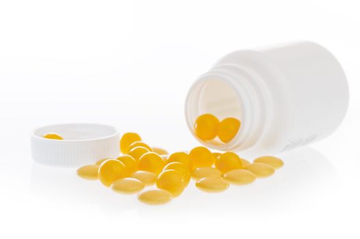 Yellow pills scattered in front of the white plastic jar.