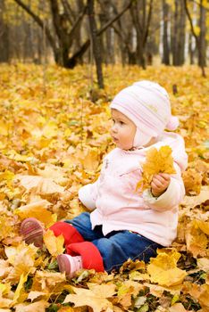 Sitting small baby playing with yellow maple leafs