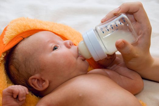 Little baby boy lying at tha bed and feeding bottle