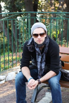 Young stylish man with scarf and beanie sitting on a bench