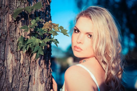 Young Blonde Woman next to a tree with a blue sky in the background