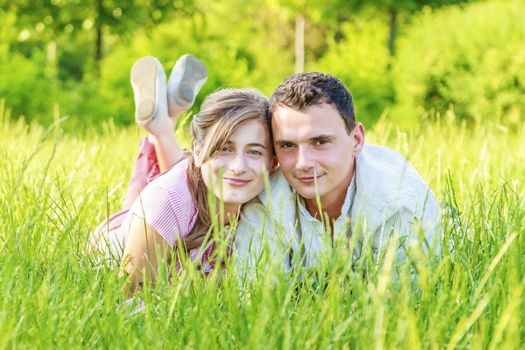 Cheerful young beautiful couple is lying in the field and enjoying the surrounding nature. 