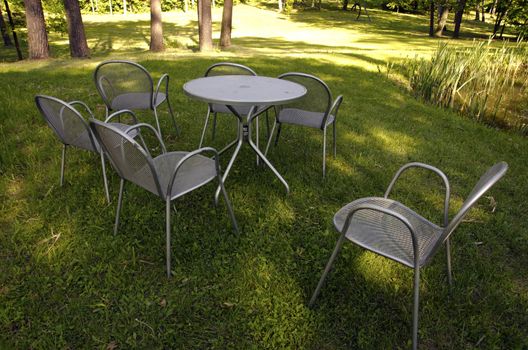 Chairs maid of metal near pond on meadow grass in garden.