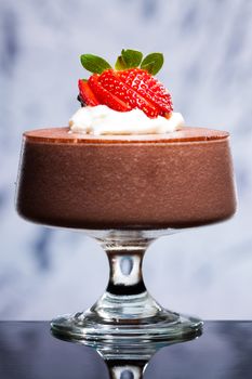 Chocolate mousse dessert with strawberries and whipped cream on a reflective surface.