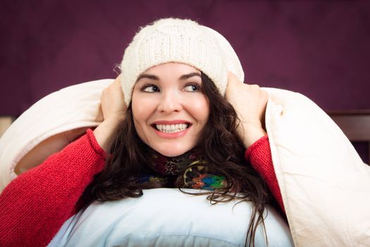 A beautiful happy young woman peeking out from underneath the blankets of her bed