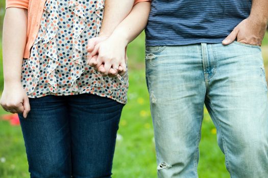 Young happy couple holding hands show at waist height showing their jeans and the womans diamond engagement ring. 