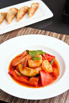 Thai style sweet and sour shrimp dish presented beautifully on a round white plate and pan fried gyoza dumplings.