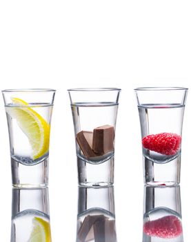 Three vodka shots flavoured with raspberry, lemon, and chocolate. Reflection in table and isolated on white.