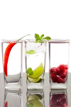 Three glasses with alcoholic drinkswith fruits and berries. On a table with refelction and isolated over white.
