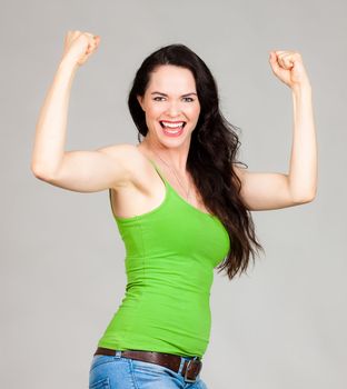 Close-up of a fit young beautiful happy woman flexing her muscles. Over grey background