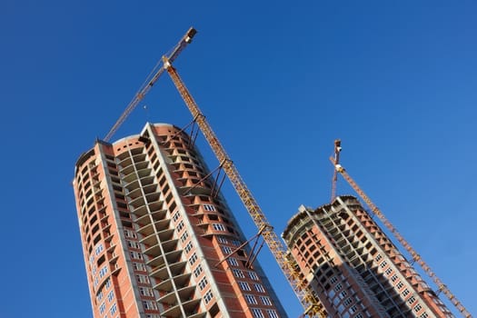 Building cranes on the construction of dwelling two parallel skyscrapers. Serene sunny day