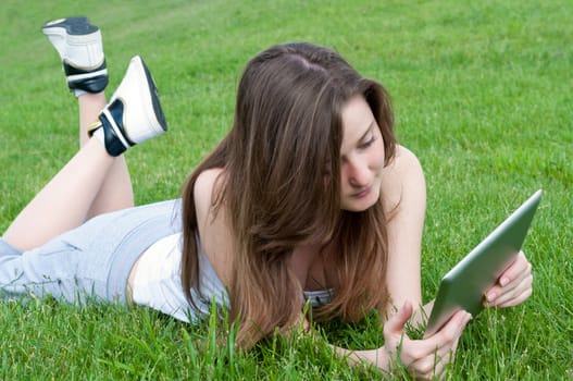 Young attractive woman lying on grass with tablet.