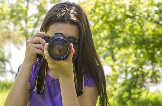 Portrait of brunette girl, making photos at summer green park.