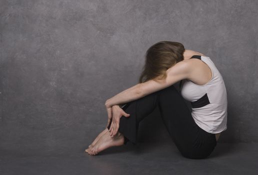 Sad woman sitting on a floor near concrete wall, studio shot