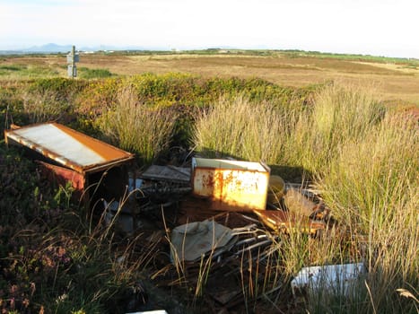 An area of moorland countryside with a pile of illegal rubbish rusting amongst grasses.