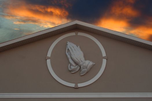 prayer hands against sunset sky