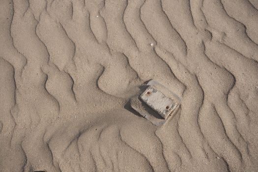 A block of wooden flotsam with rusty nails nestles amongst sand ridge shapes and textures.