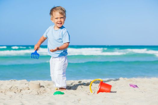 Cute baby boy playing with beach toys on tropical beach