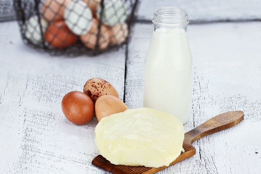 Farm fresh milk, butter, and eggs against a rustic background. Milk is in a vintage glass milk bottle. Shallow depth of field. 