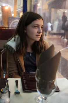 Young brunette girl waiting at a restaurant and looking calmy out of the window with a thoughtful expression